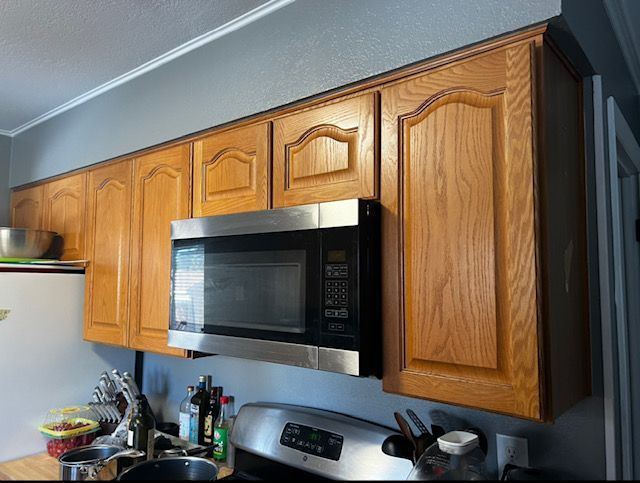 Kitchen wall cabinets with a stainless microwave above a stove and countertop items below.
