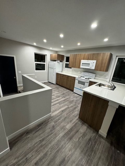 Modern kitchen with white appliances, wood cabinets, and gray flooring in an open layout