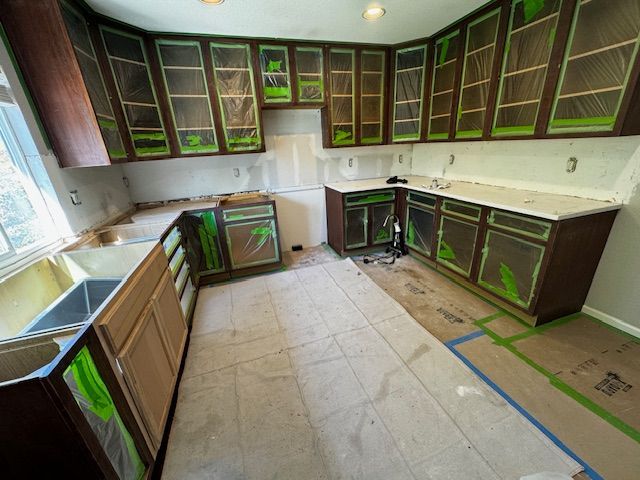 Kitchen under renovation with dark cabinets, white countertops, and taped-off floor areas