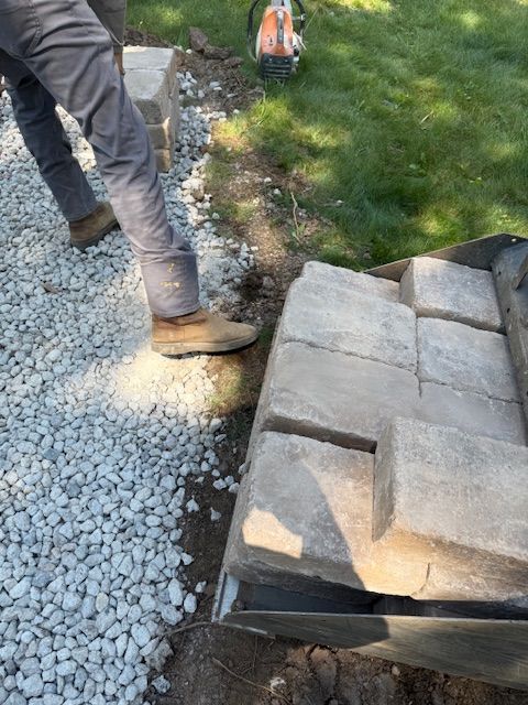 Worker placing stone pavers beside a gravel path and grass edge