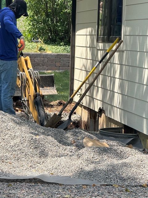 Worker using a trencher beside a house, digging a trench through gravel and soil.