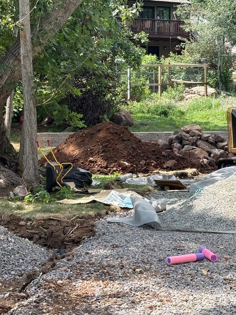 Backyard excavation site with dirt piles, gravel, tools, and a house in the background