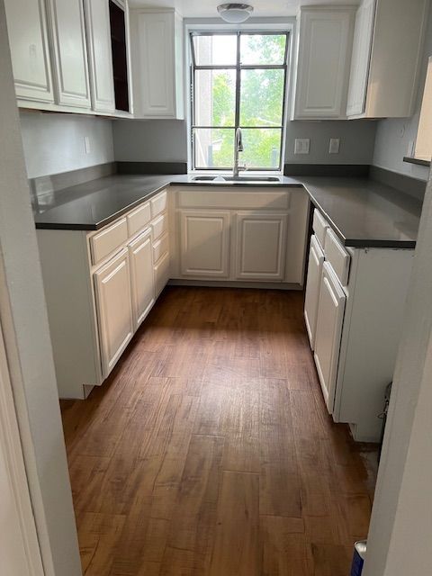 Small kitchen with white cabinets, dark countertops, wood floor, and a window over the sink.