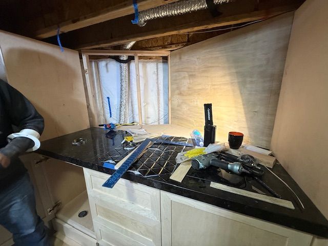 Worker installing a dark countertop in an unfinished kitchen with tools and cabinets.