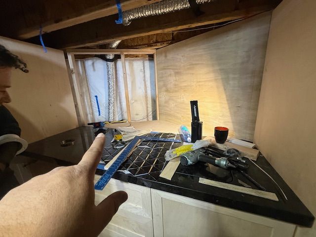 Hand pointing at a workbench with tools, tape measures, a drink, and a dimly lit window backdrop