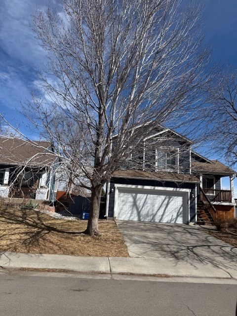 Suburban two-story house with a garage, leafless tree, and driveway under a blue sky