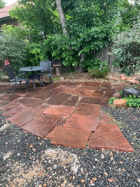 Patio with red stone pavers, gravel edges, and a small outdoor table and chairs under trees