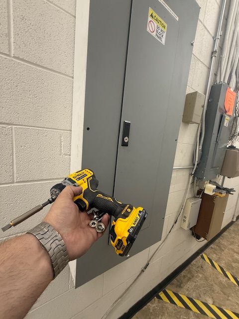 Hand holding a yellow drill near a gray electrical panel in a utility hallway