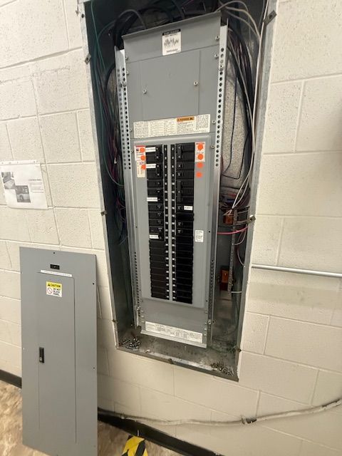 Open electrical breaker panel in a wall recess beside a gray utility cabinet.