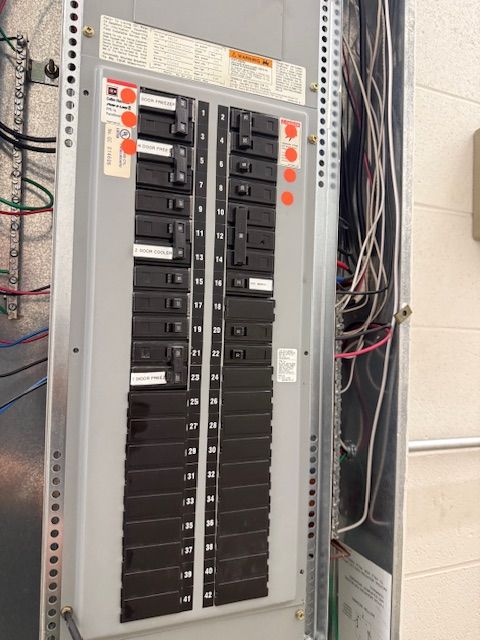 Open electrical breaker panel with rows of black circuit breakers and exposed wiring.