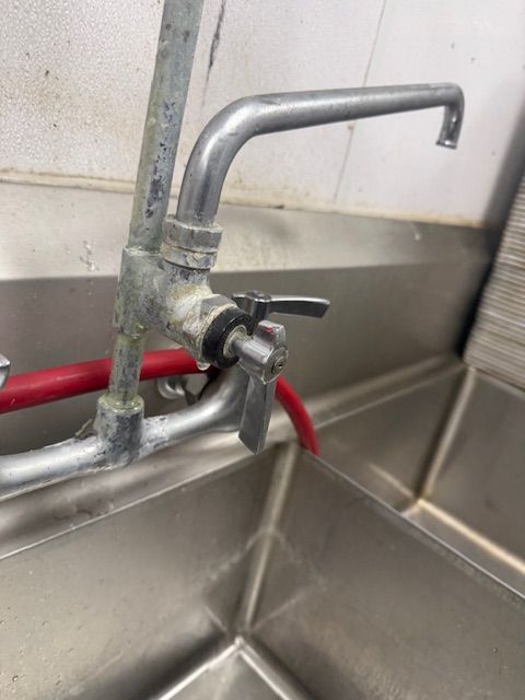 Close-up of a metal sink faucet and red hose in a stainless steel utility sink.