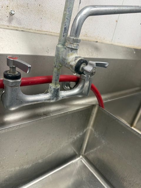 Kitchen sink faucet with a red hose attached, filling a stainless steel sink.