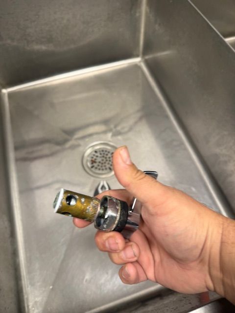 Hand holding a small metal sink faucet part over a stainless steel sink drain