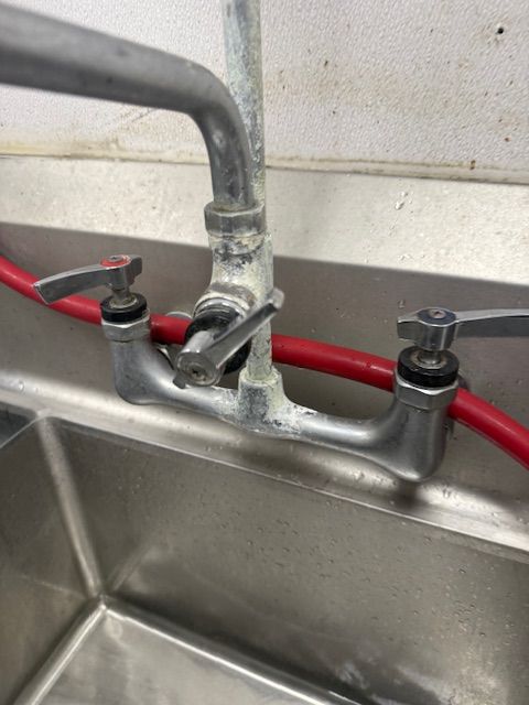 Industrial sink with a worn faucet and red hose against a stainless steel backsplash