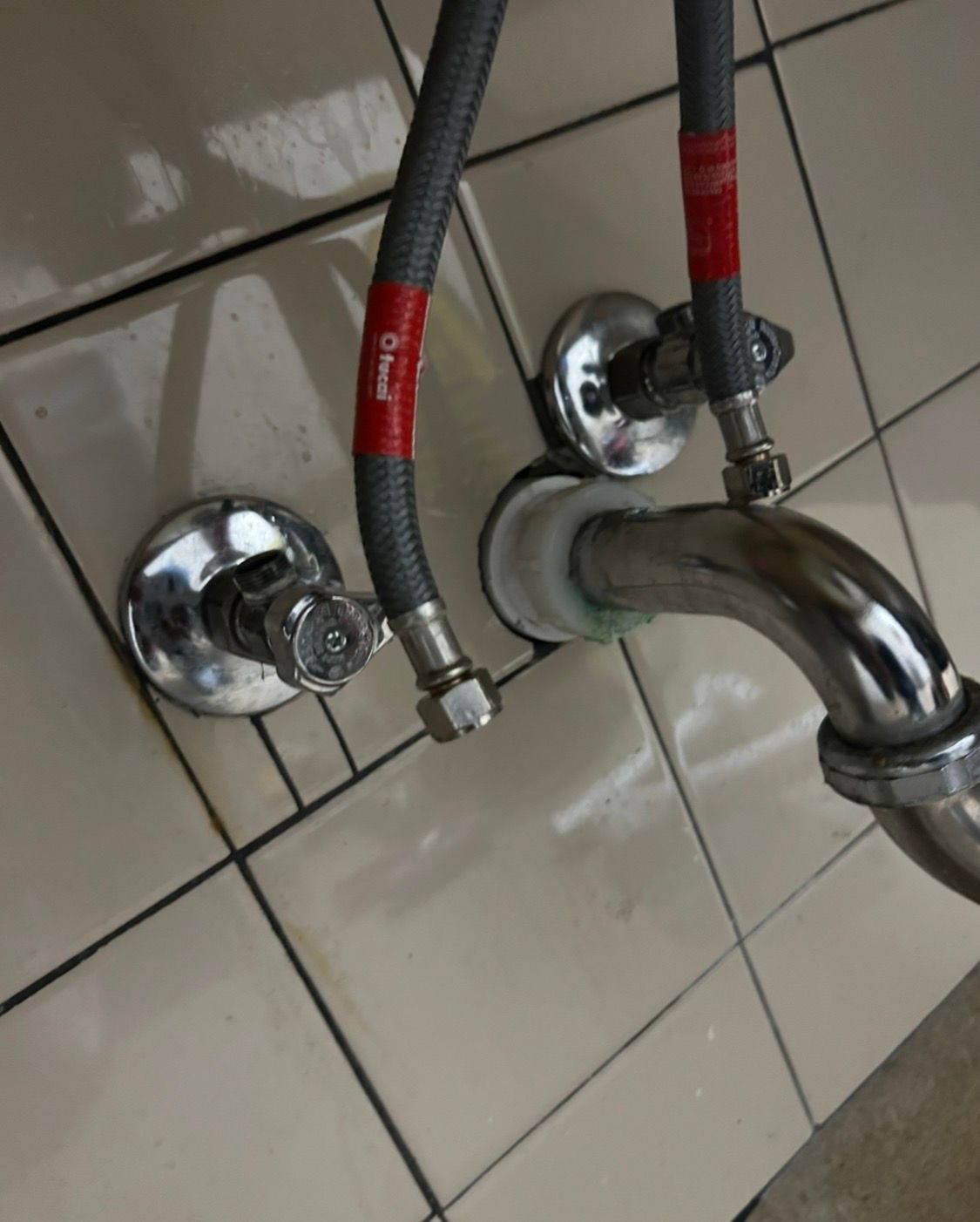 Chrome bathroom faucet and two braided supply lines mounted on tiled wall