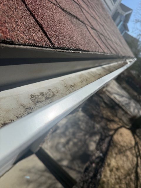 Close-up of a roof edge with white gutter and red shingles in sunlight