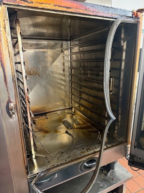 Open metal smoker or oven with charred interior and a partially open door