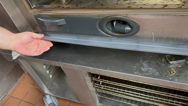Hand reaching toward a dirty metal vent or appliance panel with an oval handle on a tiled surface