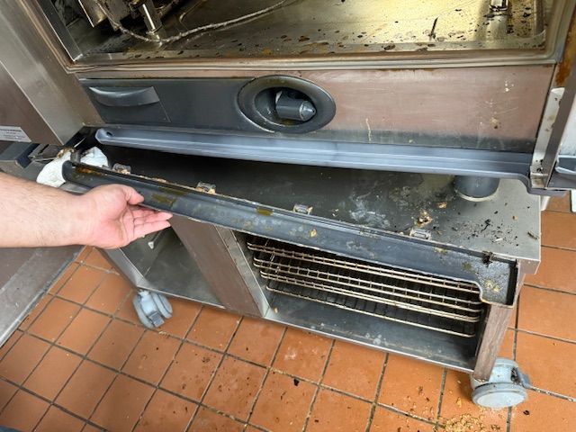 Hand reaching toward a stainless-steel oven door in a commercial kitchen