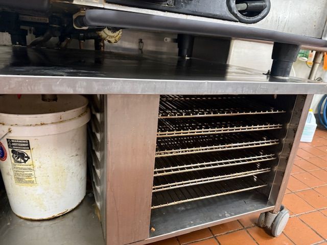 Commercial kitchen rack with trays, white bucket, and stainless steel countertop on wheels