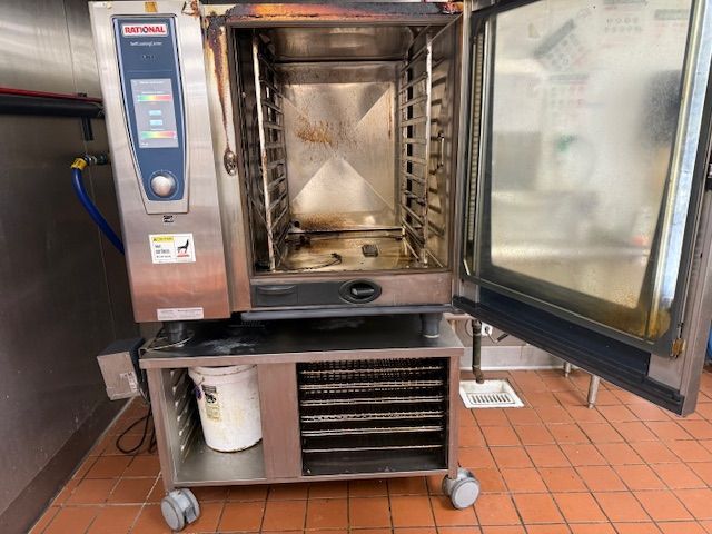 Large commercial stainless-steel oven with open door in a tiled kitchen or bakery.