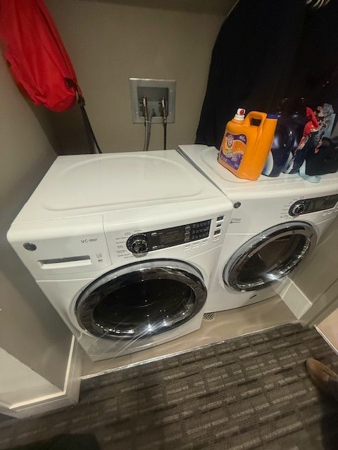 Laundry room with stacked white washer and dryer, orange detergent on top, and a floor drain in front