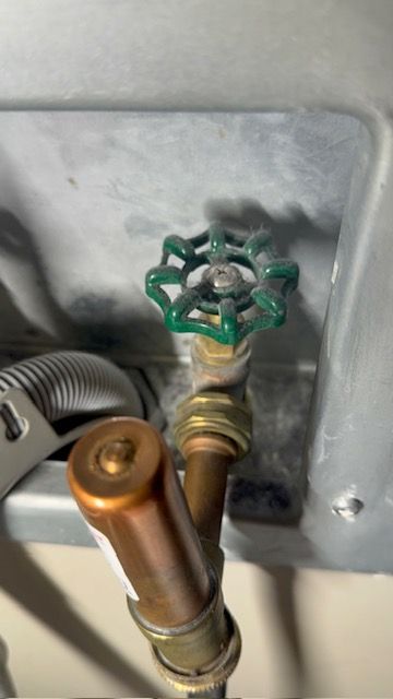 Green-handled water shutoff valve on a pipe inside a gray utility panel