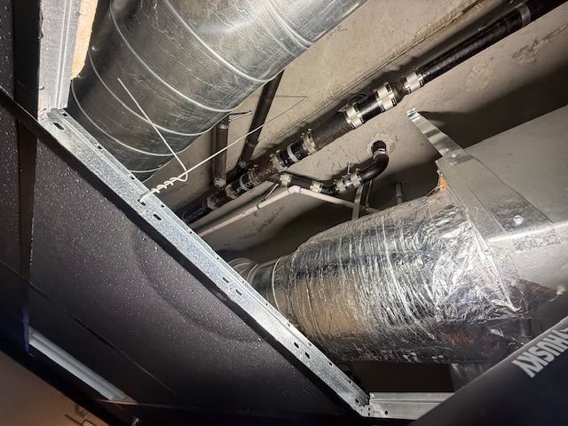 Metal ductwork and insulated HVAC pipes running across a ceiling in an industrial space