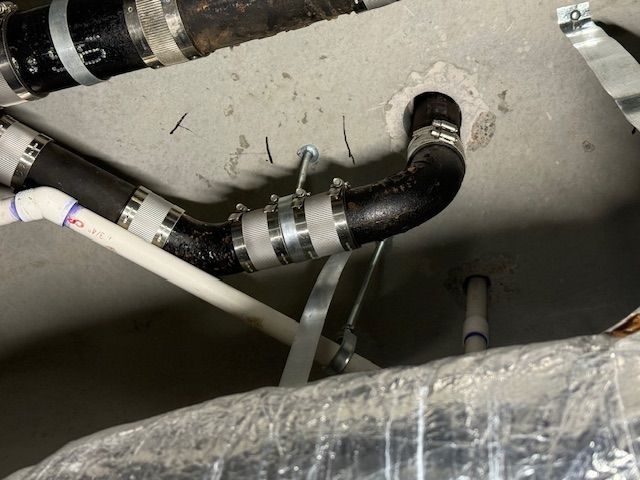 Black insulated pipe with metal clamps inside a ceiling utility space