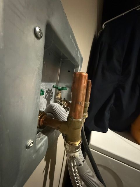 Close-up of copper plumbing pipes and hoses beside a washing machine and wall panel