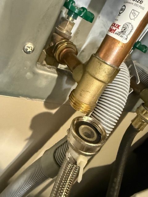 Close-up of plumbing connections with braided hose, brass fittings, and green valve in a utility space