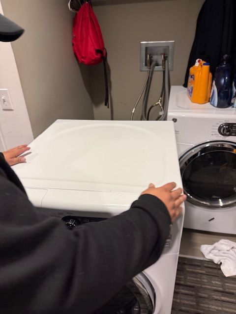 Person placing a white dryer cover in a laundry room next to a washer and detergent bottles