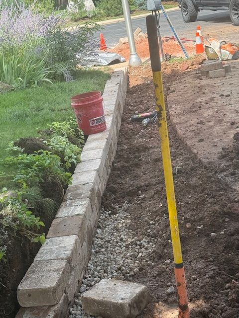 Construction site with curbing, orange cones, and a yellow measuring pole along a dirt trench