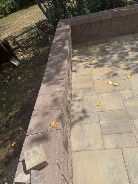 Stone patio corner with low brick wall, scattered yellow leaves, and a shady outdoor area nearby