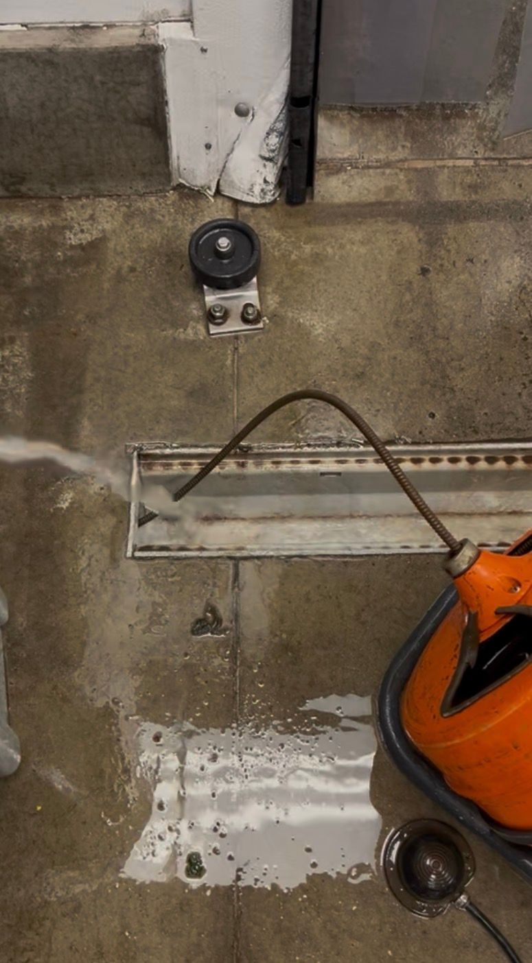 Orange wet/dry vacuum cleaning a wet concrete floor near a wall and floor drain