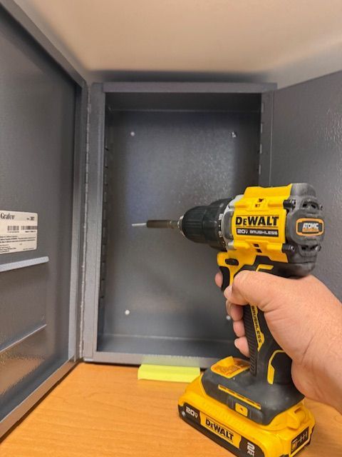 Hand holding a yellow DeWalt drill inside an open gray metal cabinet