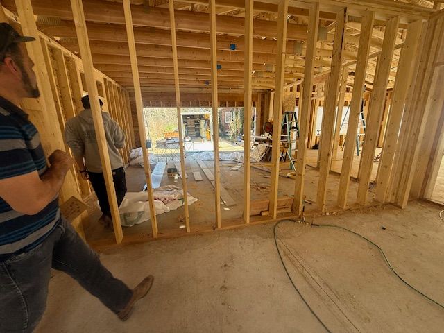 Interior of a house under construction with exposed framing and two workers standing near a doorway