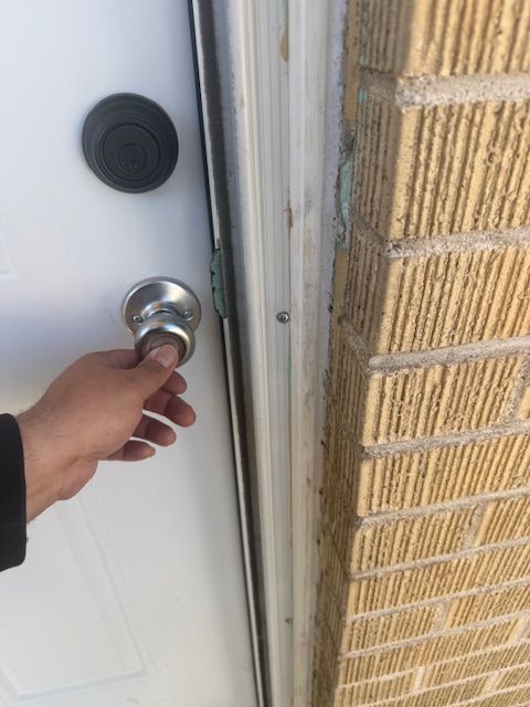 Hand turning a silver front-door knob beside a brick wall and white door frame