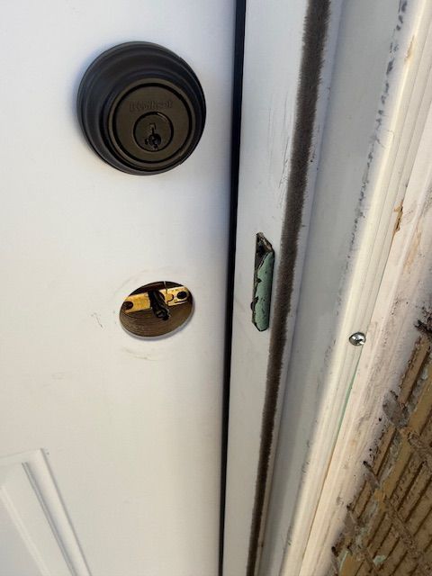 Close-up of a white door cracked open, showing the deadbolt, latch, and door frame.
