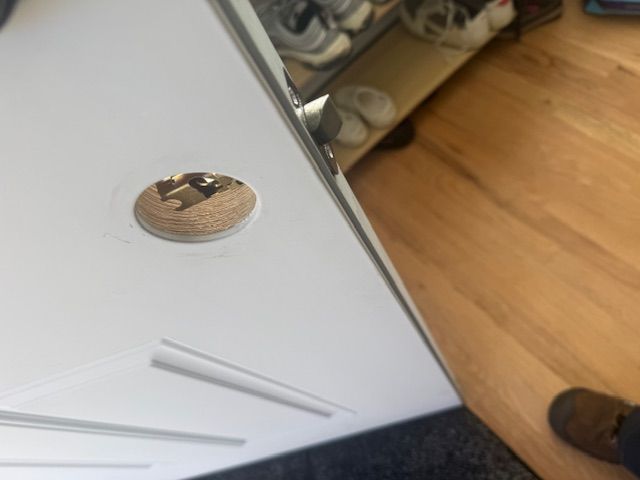 Tilted view of a white cabinet door and wood floor, with a brown shoe visible at the right edge.