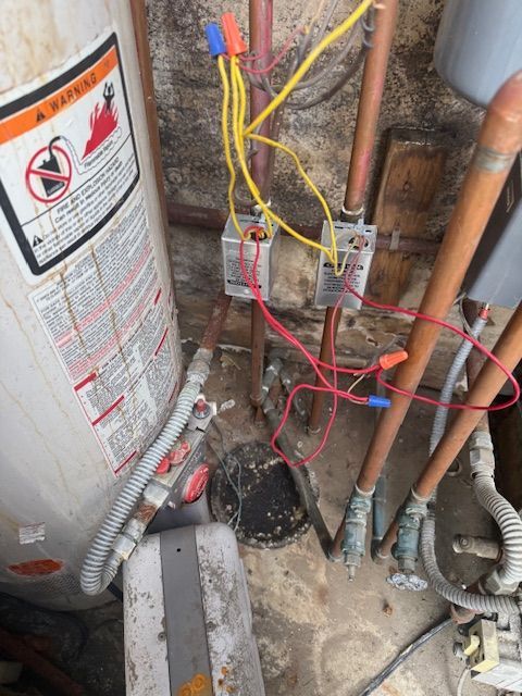 Water heater with exposed red and yellow wiring, copper pipes, and ducting in a utility closet.
