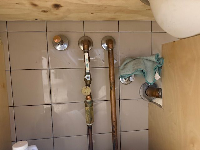 Under-sink plumbing with copper pipes, tiled wall, and a cloth tucked beside a cabinet
