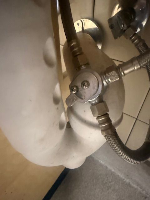 Close-up of a bathroom sink drain with metal plumbing and flexible hoses under a white basin