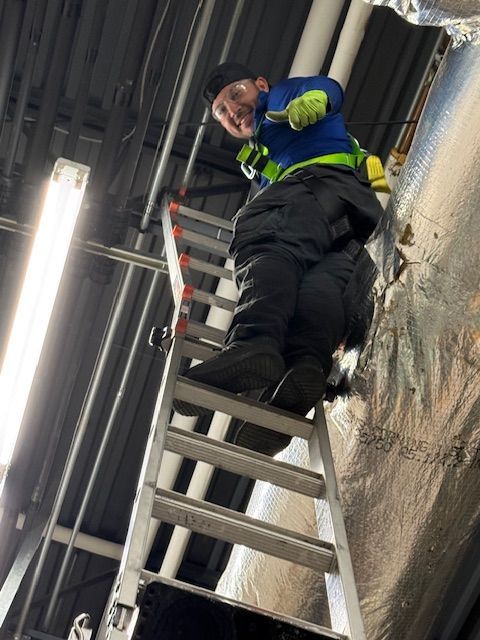 Worker in blue and green safety gear climbing a ladder in an industrial stairwell.