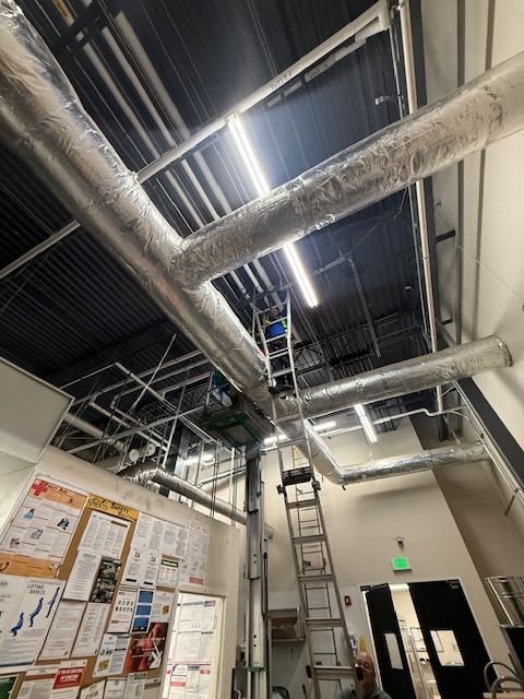 Industrial utility room with exposed ceiling pipes, fluorescent lights, bulletin board, and exit door
