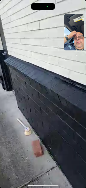 White clapboard building with black lower siding and a small inset selfie in the upper right.