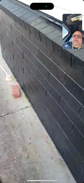 Black brick wall along a sidewalk, with a small circular inset of a person’s face in the corner