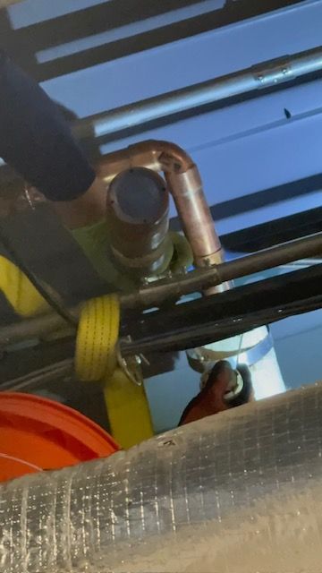 Close-up of copper pipes and black cables beneath a blue surface, with a yellow strap and orange bucket visible