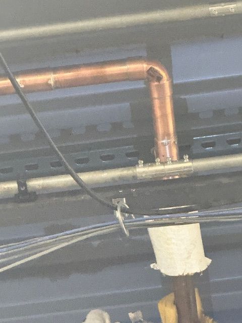 Copper pipe and black cables running along a ceiling, with a white insulated section below.