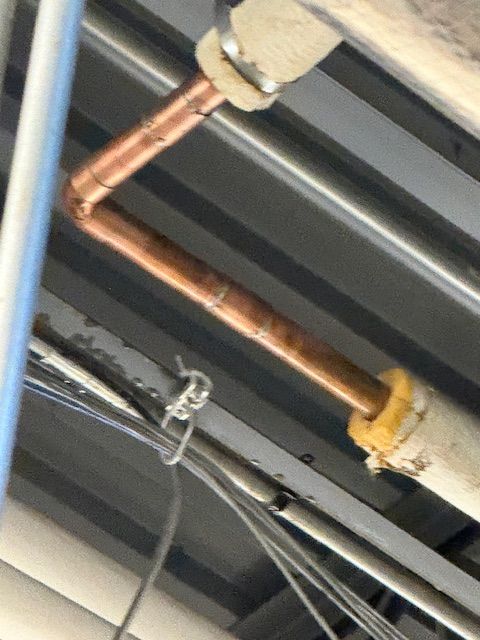 Copper pipe and fittings running along a metal ceiling with a yellow joint